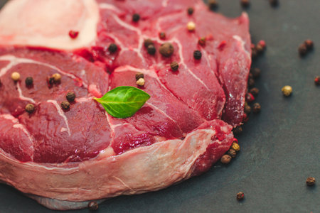 Fresh piece of meat large beef steak on the bone ossobuco with a sprig of rosemary on a black background.の写真素材