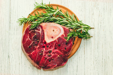 Fresh piece of meat large beef steak on the bone ossobuco with pepper, rosemary on the board.の写真素材