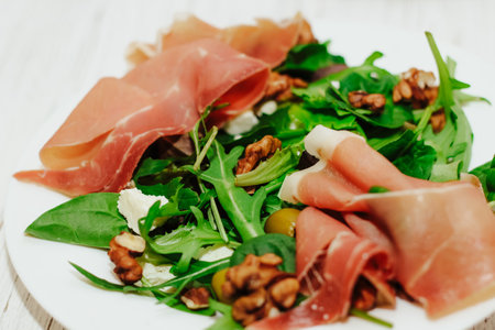 Salad with herbs, arugula, prosciutto, cheese, green olives and nuts.の写真素材