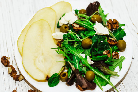 Salad with pears, herbs, arugula, prosciutto, cheese, green olives and nuts.の写真素材