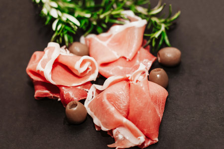 Pieces of dried pork jamon prosciutto with olives on a black board.の写真素材