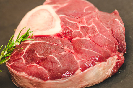 Fresh piece of meat large beef steak on the bone ossobuco with a sprig of rosemary on a black background.の写真素材