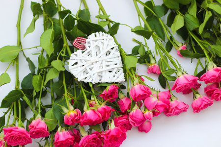 Decorative white heart made of vines, Valentine's Day on the background of a bouquet of roses.の写真素材