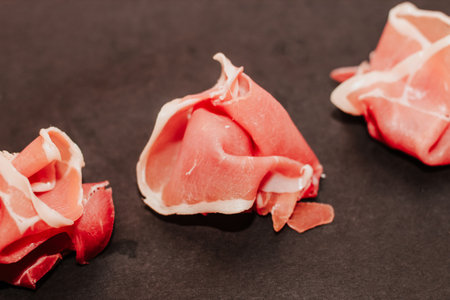 Pieces of dried pork jamon prosciutto on a black board.の写真素材
