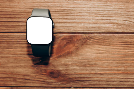 A black technological smart watch lies on a wooden background with a white screen for text spaceの写真素材