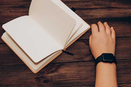 A black technological smart watch lies on a notepad for time management.の写真素材