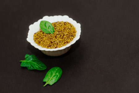 grain mustard with a green leaf in a white bowl on a black background.の写真素材