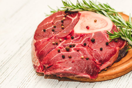 Fresh piece of meat large beef steak on the bone ossobuco with pepper, rosemary on the board.の写真素材