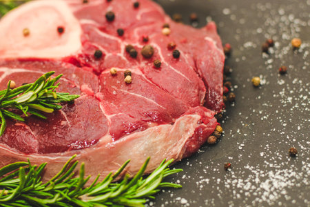 Fresh piece of meat large beef steak on the bone ossobuco with a sprig of rosemary on a black background.の写真素材
