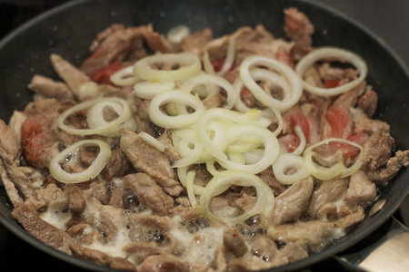 Chopped pieces of pork are fried in a pan with onions cut into rings.の写真素材