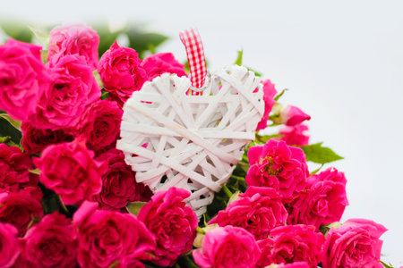 Decorative white heart made of vines, Valentine's Day on the background of a bouquet of roses.の写真素材