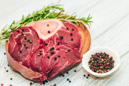 Fresh piece of meat large beef steak on the bone ossobuco with pepper, rosemary on the board.の写真素材