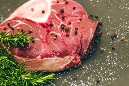 Fresh piece of meat large beef steak on the bone ossobuco with a sprig of rosemary on a black background.の写真素材