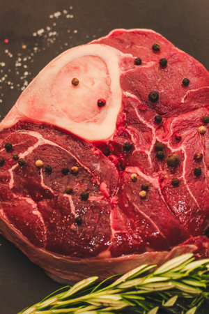 Fresh piece of meat large beef steak on the bone ossobuco with a sprig of rosemary on a black background.の写真素材