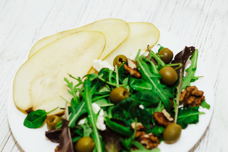 Salad with pears, herbs, arugula, prosciutto, cheese, green olives and nuts.の写真素材