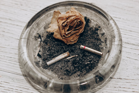 Ashtray with cigarette butts and a dry rose, the concept of parting and sadness.の写真素材