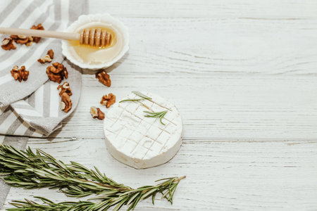 Round cheese in camembert mold with a sprig of rosemary, honey and nuts on the table.の写真素材