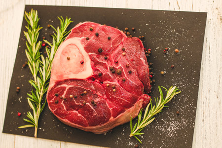 Fresh piece of meat large beef steak on the bone ossobuco with a sprig of rosemary on a black background.の写真素材
