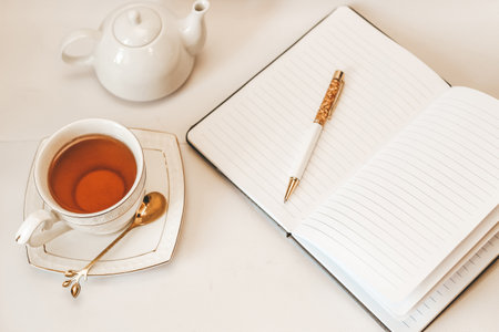 White cup and saucer with golden spoon and teapot and notepad.の写真素材