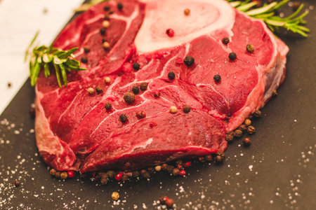Fresh piece of meat large beef steak on the bone ossobuco with a sprig of rosemary on a black background.の写真素材