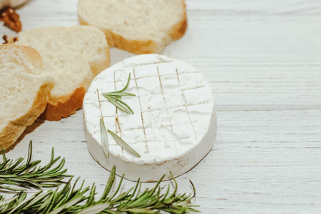 Round cheese in camembert mold with a sprig of rosemary, honey and nuts on the table.の写真素材