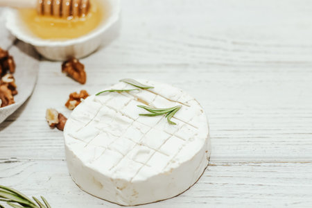 Round cheese in camembert mold with a sprig of rosemary, honey and nuts on the table.の写真素材