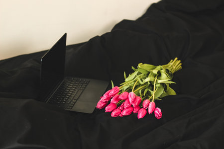 A bouquet of pink flowers on black stylish linen with an open laptopの写真素材