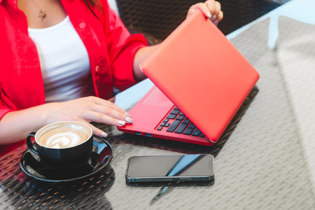 A girl in works on a laptop in a cafe with a cappuccino and a phoneの写真素材