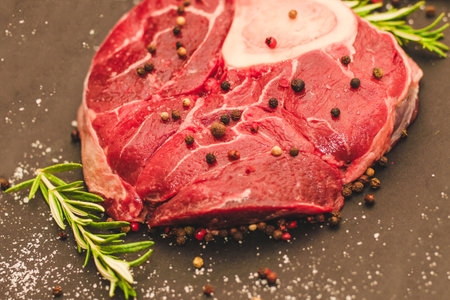 Fresh piece of meat large beef steak on the bone ossobuco with a sprig of rosemary on a black background.の写真素材