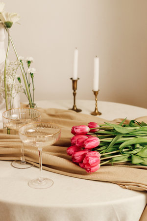 Stylish romantic table setting in the interior with glasses and a bouquet of tulipsの写真素材