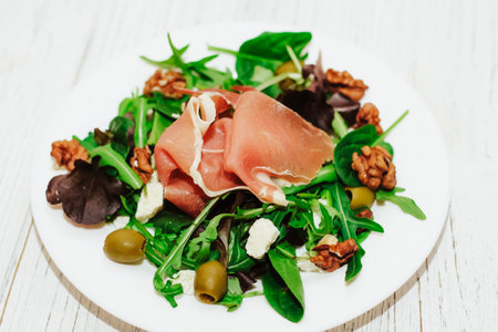 Salad with herbs, arugula, prosciutto, cheese, green olives and nuts.の写真素材