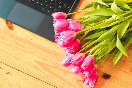 A bouquet of pink tulips flowers on a background of boards with an open laptopの写真素材