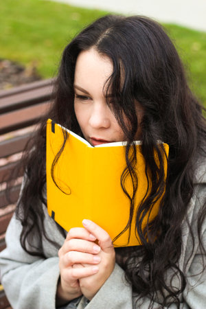 stylish curly girl in a coat with a yellow diaryの写真素材