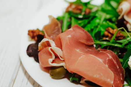 Salad with herbs, arugula, prosciutto, cheese, green olives and nuts.の写真素材