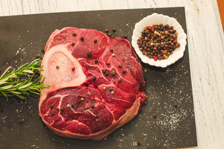 Fresh piece of meat large beef steak on the bone ossobuco with a sprig of rosemary on a black background.の写真素材