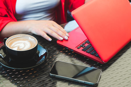 A girl in works on a laptop in a cafe with a cappuccino and a phoneの写真素材