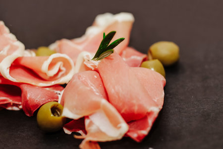 Pieces of dried pork jamon prosciutto with olives on a black board.の写真素材