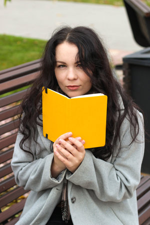 stylish curly girl in a coat with a yellow notebookの写真素材