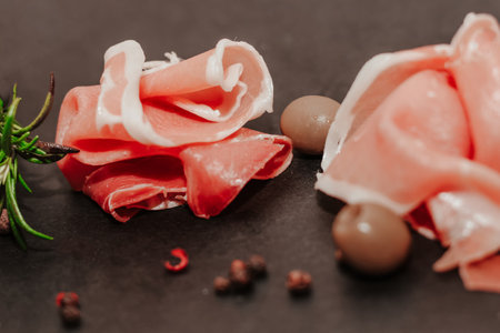 Pieces of dried pork jamon prosciutto with olives on a black board.の写真素材