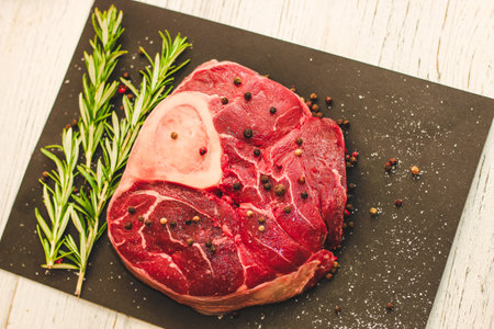 Fresh piece of meat large beef steak on the bone ossobuco with a sprig of rosemary on a black background.の写真素材