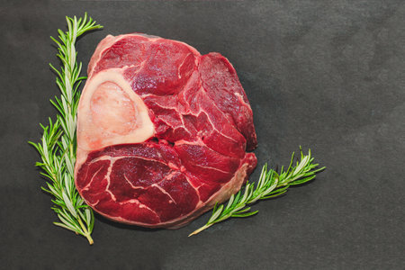 Fresh piece of meat large beef steak on the bone ossobuco with a sprig of rosemary on a black background.の写真素材