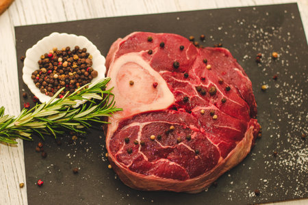 Fresh piece of meat large beef steak on the bone ossobuco with a sprig of rosemary on a black background.の写真素材