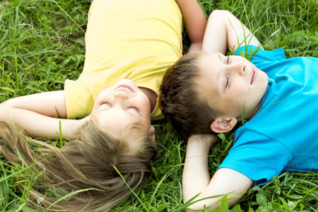 Children are lying on the grass, their clothes are yellow and blue.の写真素材