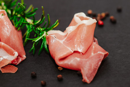 Pieces of dried pork jamon prosciutto with rosemary on a black board.の写真素材