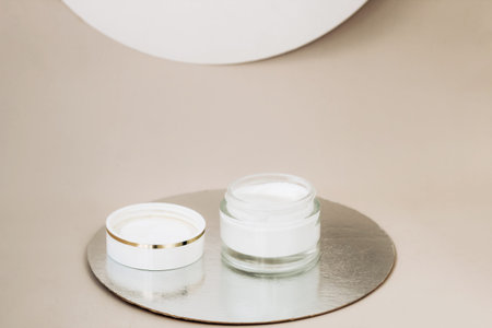 Facial care cream in a glass jar on a beige background