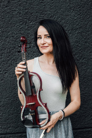 A woman artist with dark hair in a dress holds a wooden concert electric violin in her handsの写真素材