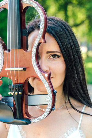 A woman artist with dark hair in a dress holds a wooden concert electric violin in her handsの写真素材
