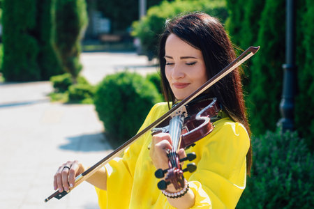 Woman artist with dark hair in a dress plays a wooden concert electric violinの写真素材