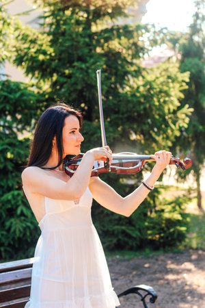 Woman artist with dark hair in a dress plays a wooden concert electric violinの写真素材