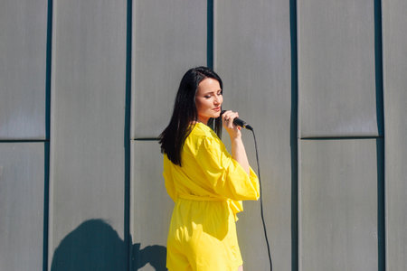 Woman vocalist with dark hair in a dress sings into a microphoneの写真素材